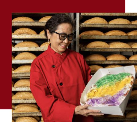 image of Mrs. Tran, owner of Dong Phuong Bakery holding a king cake against a backdrop of trays of French bread